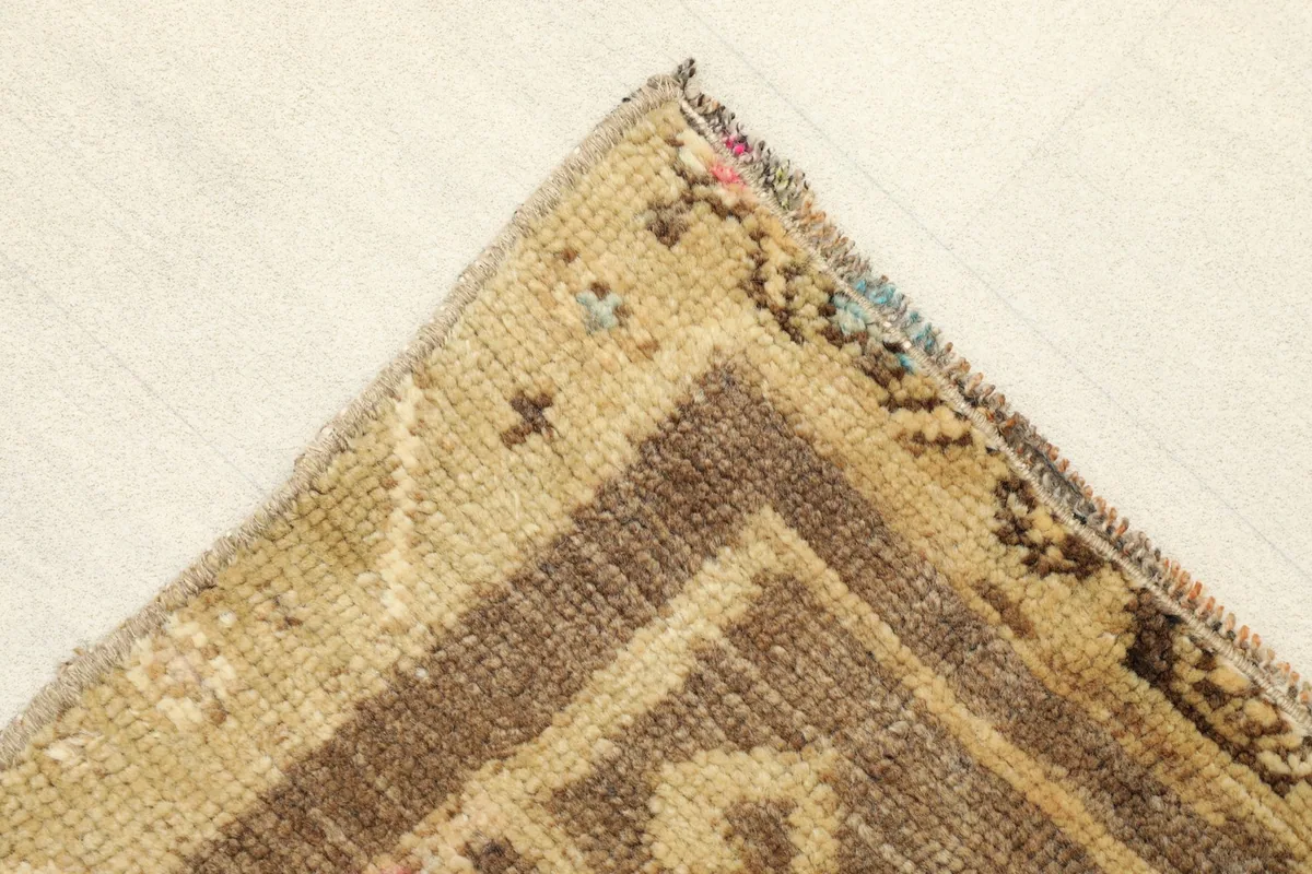Corner detail of the rug, showing the brown border and tan field with subtle patterns.