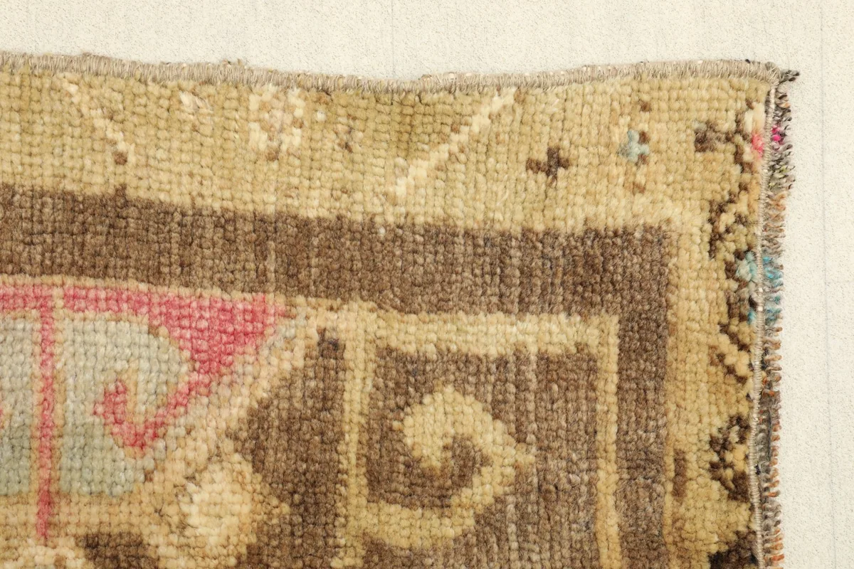 Edge view of the vintage doormat, displaying the hand-knotted construction and border design.