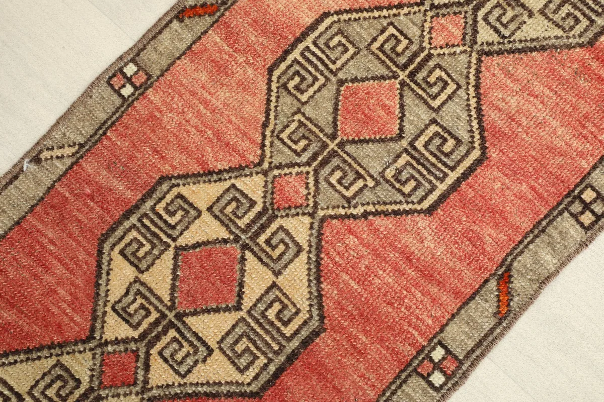 Close-up detail of the central geometric pattern with rose, beige, and gray elements in the vintage rug.