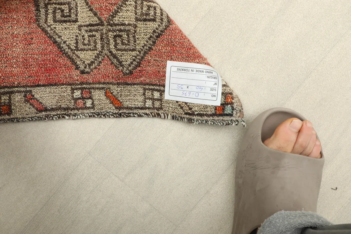 Back of the rug with a label, demonstrating the hand-knotted foundation and construction details next to a foot.