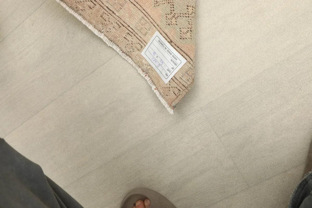A partial view of the rug on the floor next to human feet for scale