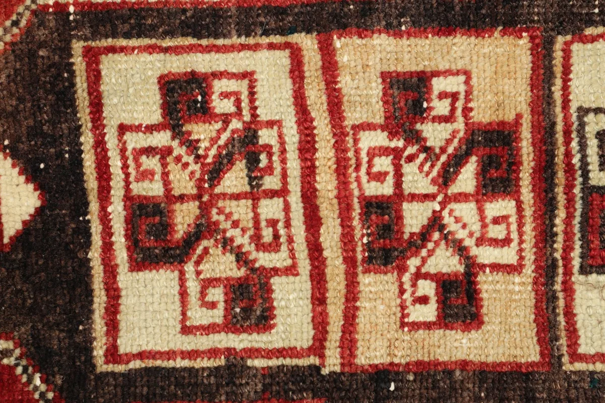 Macro detail showing the intricate red and brown geometric patterns within an ivory square motif.