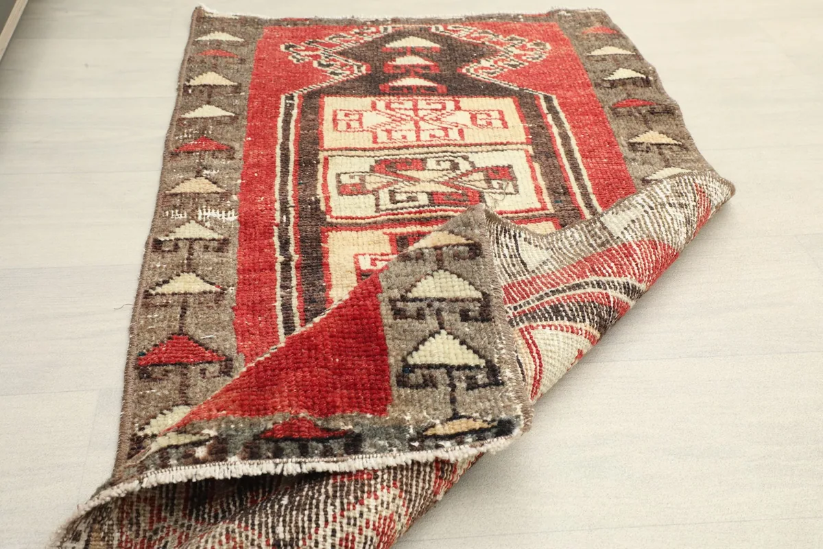 The red and gray doormat folded to reveal its back and the thickness of the wool pile.