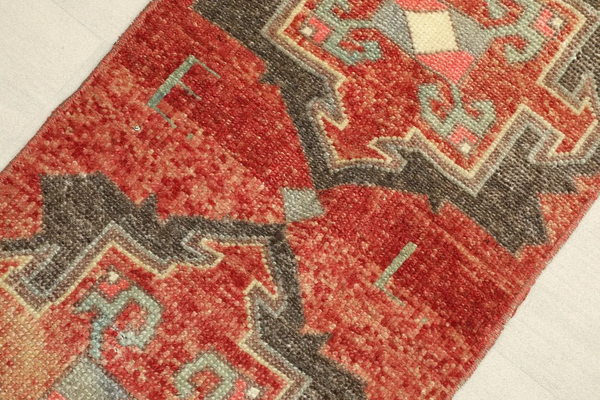 Close-up detail of the rug's surface, showing the rich red wool pile and geometric motifs.