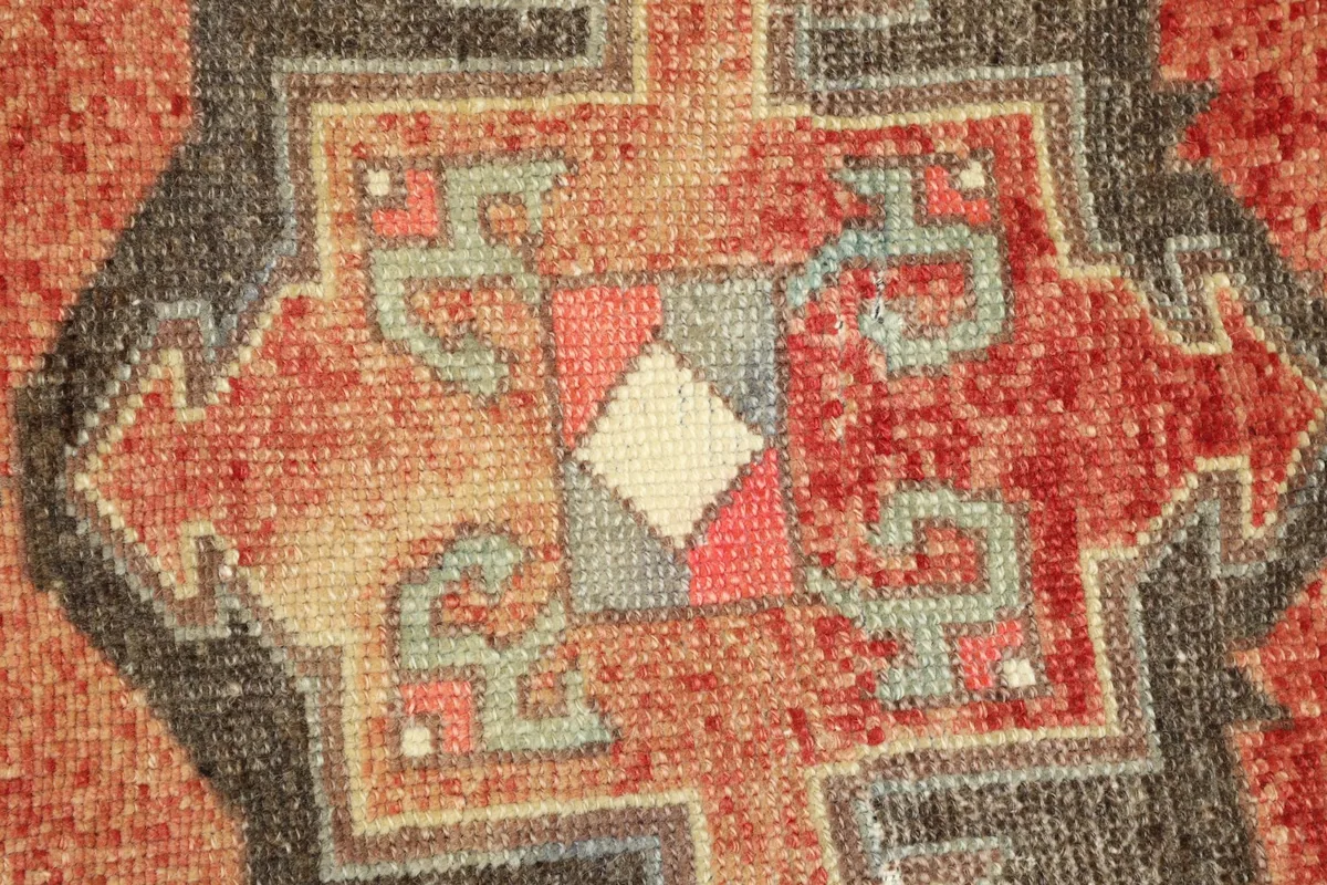 Detailed view of a central geometric motif in charcoal, beige, and gray against the red field.