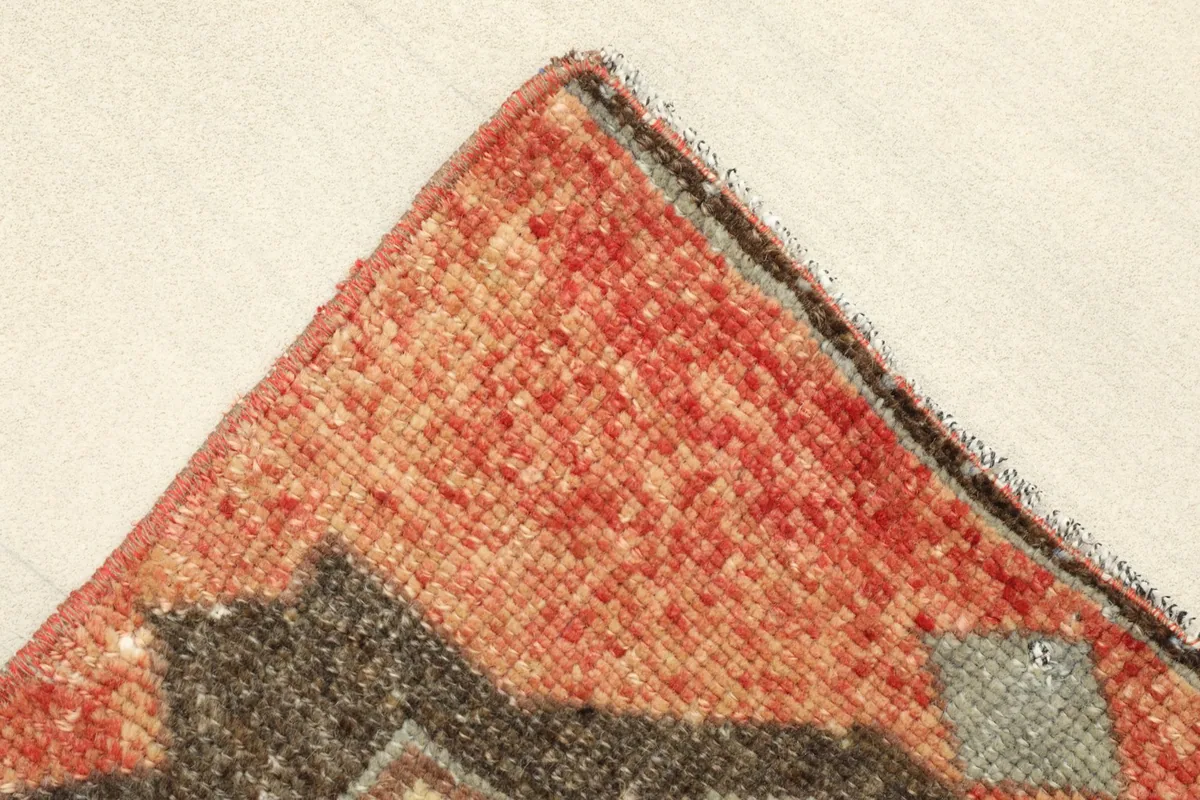 Corner detail of the rug, showing the hand-knotted edge and slight variations in the red pile.
