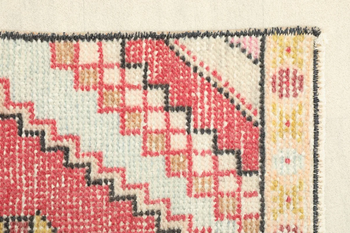 Close-up of the geometric patterns in the corner, with rose, cream, and light blue tones.