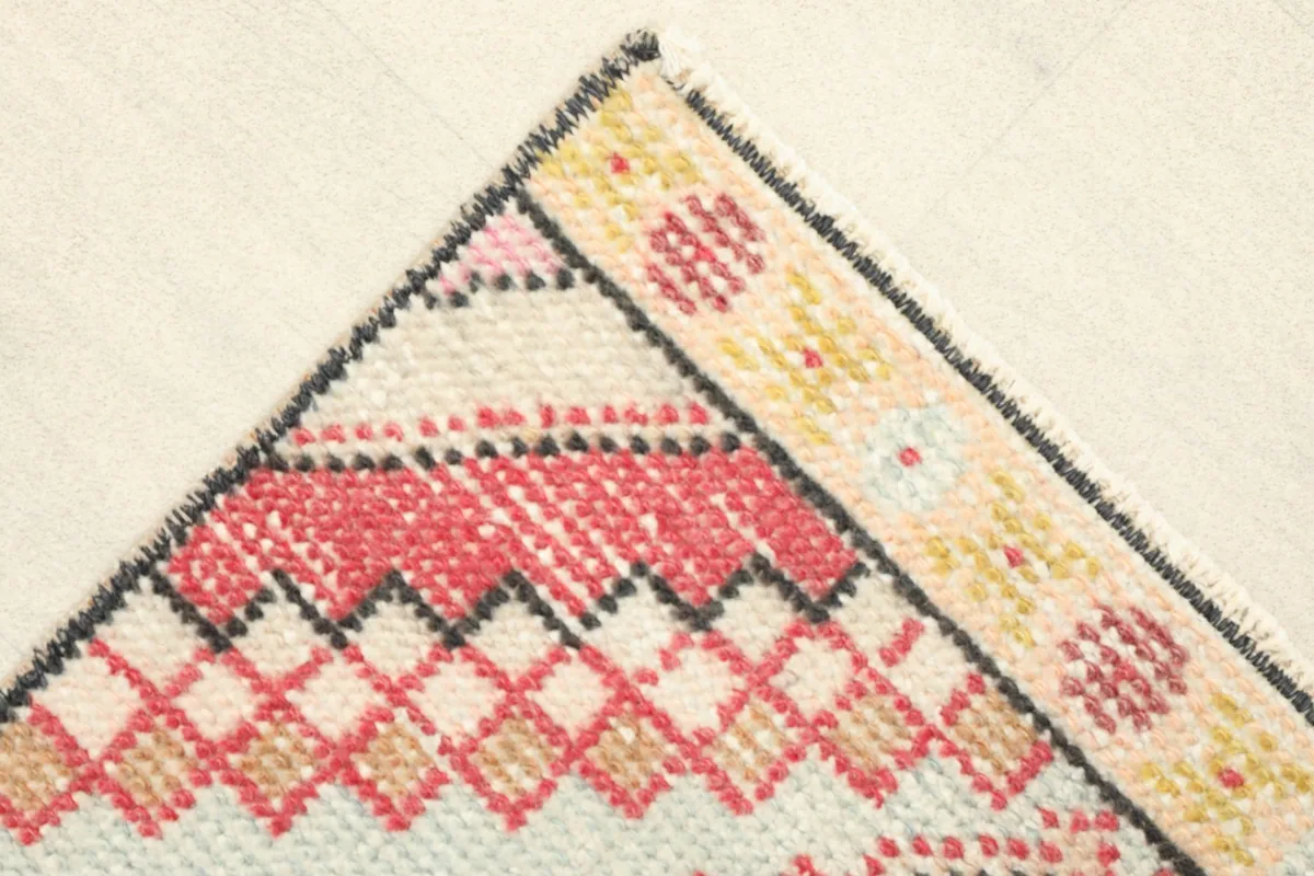 Corner detail showing the patterned border in yellow, cream, and pink, and the hand-knotted edge.