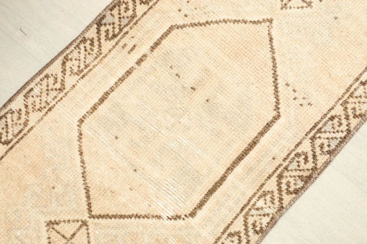 Angled view highlighting the tan field and the distinct brown tribal border of the hand-knotted rug