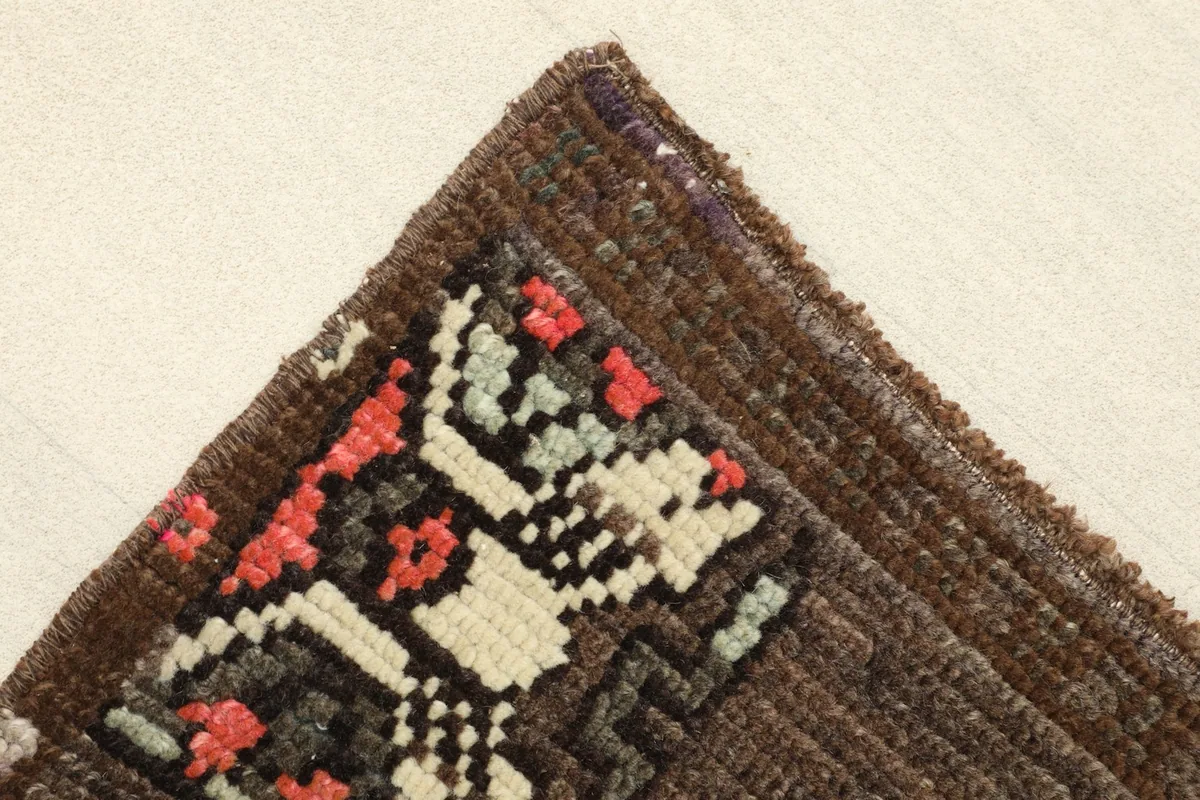 Corner detail showing the tight weave and the edge of a tribal motif in rose, ivory, and black.