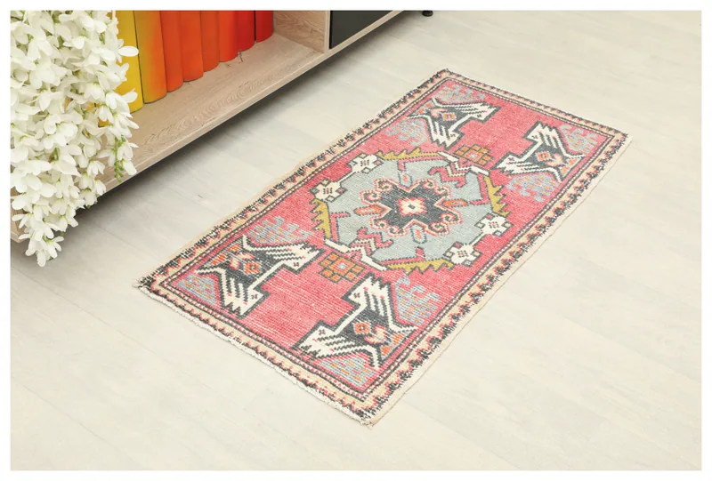 Full overhead view of the vintage rose and blue geometric tribal doormat on a light floor.