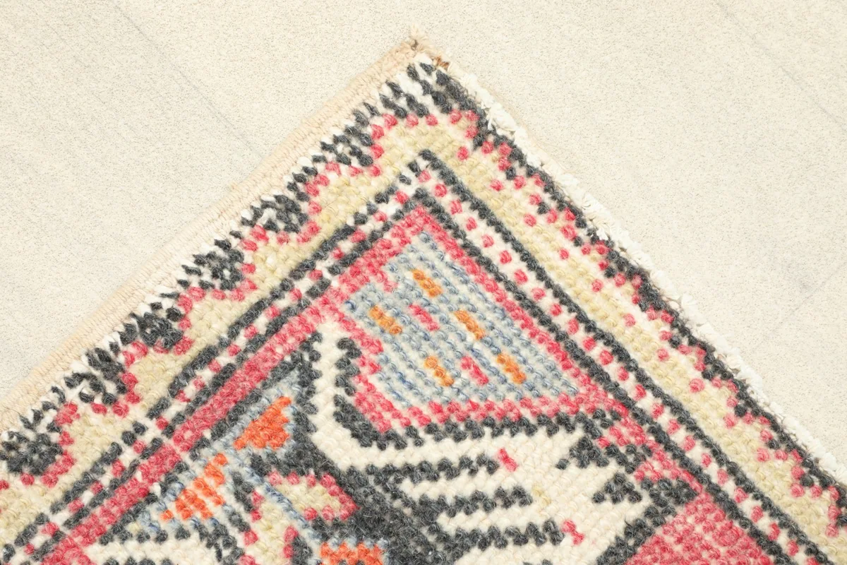 Corner detail of the doormat, showing the geometric border design and faded colors of the wool pile.