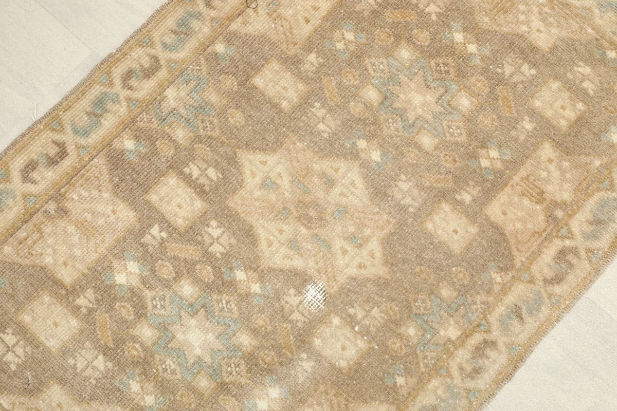 Angled close-up of the vintage rug's tan, brown, and blue geometric design