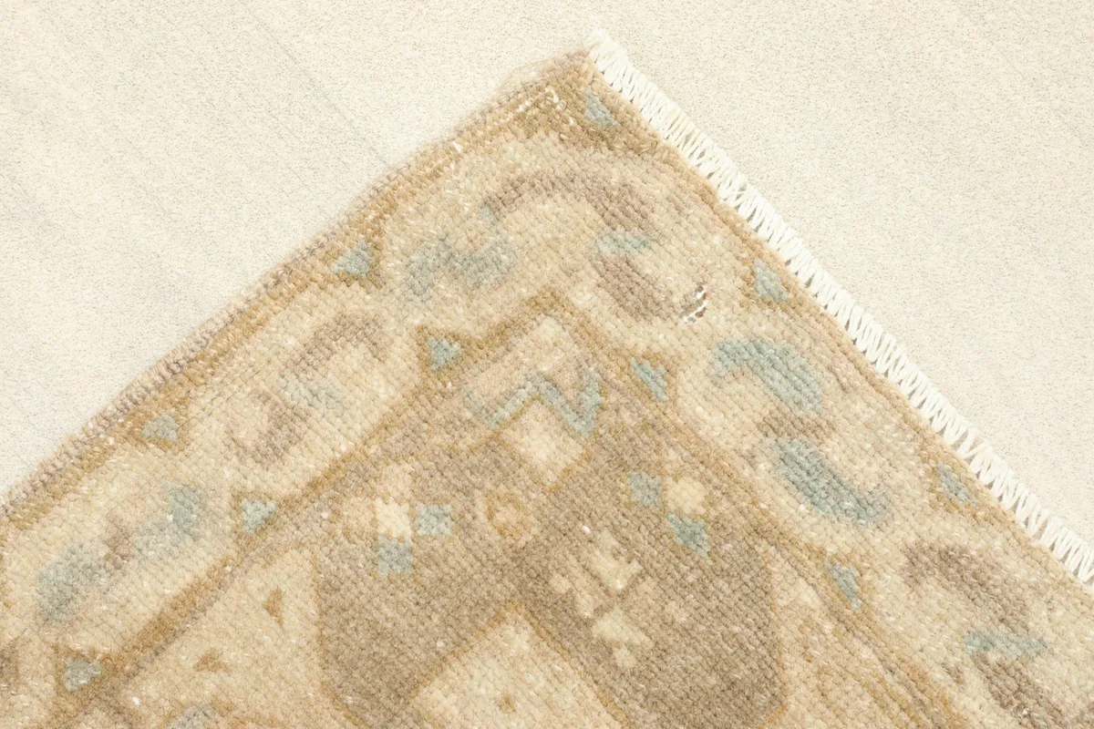 Corner detail of the rug's border pattern in tan and brown with blue accents
