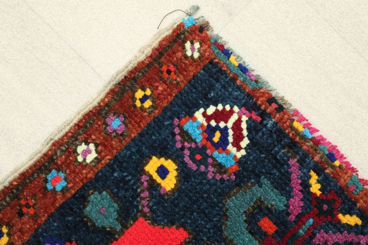 Corner detail showing the rust border with small multicolor accents and the rug's edge