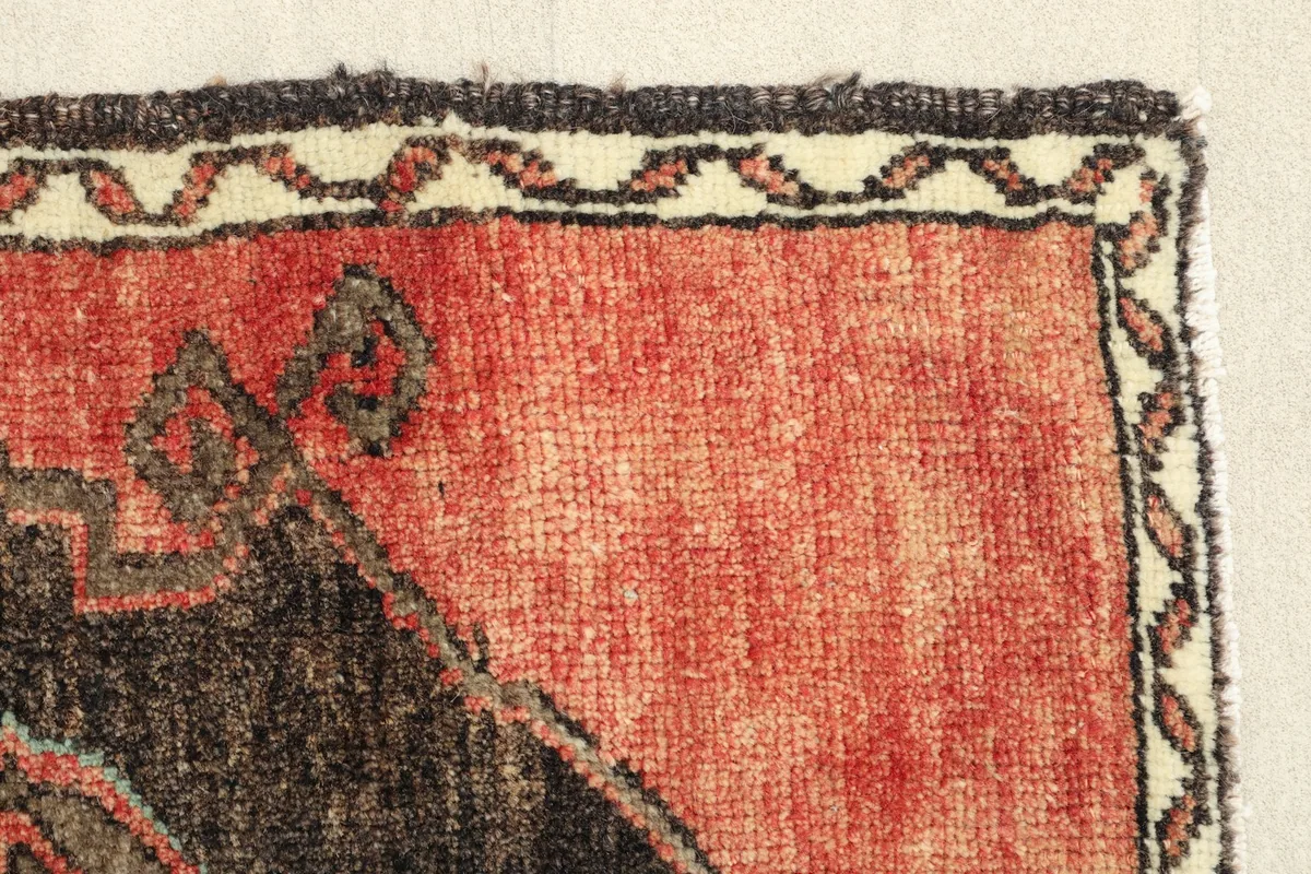 Detailed view of the rug's edge, showing the red field and the intricate border pattern.