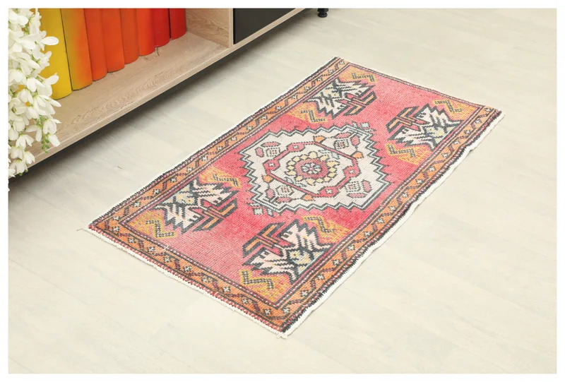 Full top view of a rose colored Anatolian doormat with an ivory medallion and geometric patterns