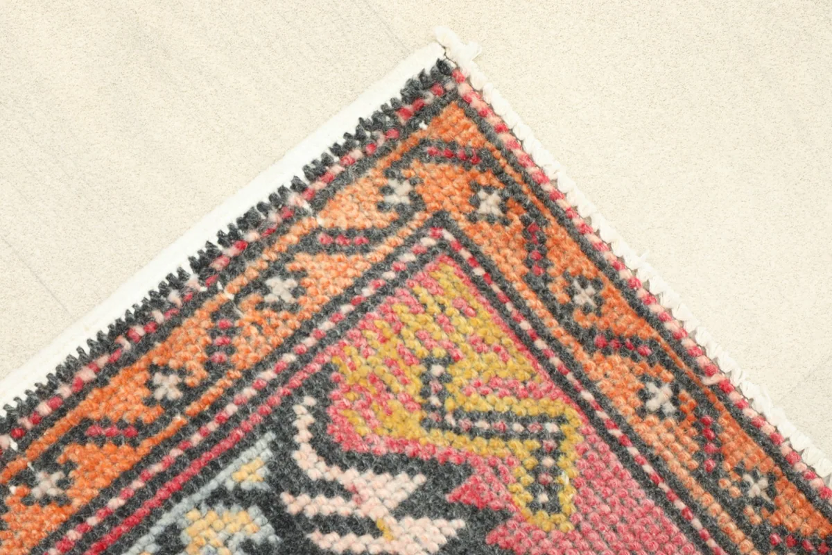 Corner detail showing the orange and charcoal geometric border design of the rug