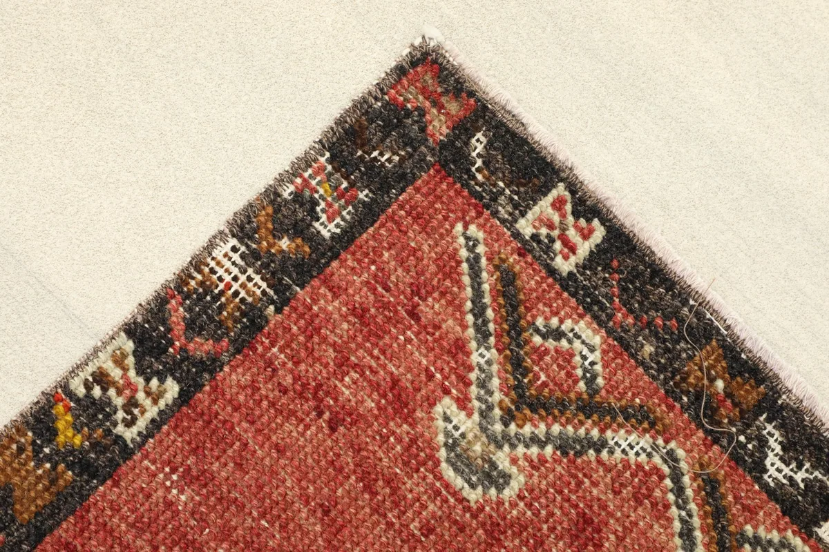 Corner detail of the rug, showing the rust field, cream elements, and dark geometric border.