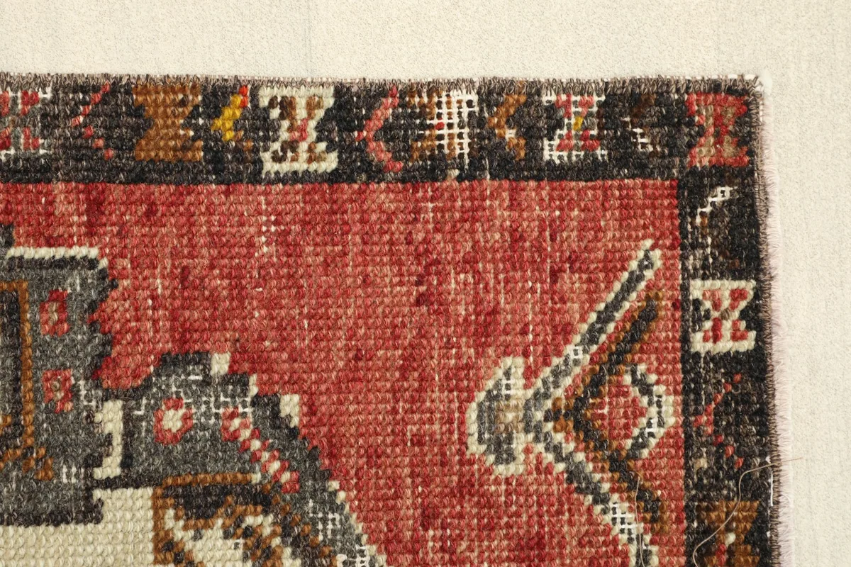 Edge detail of the rug, highlighting the rustic rust color and the dark, intricate border pattern.