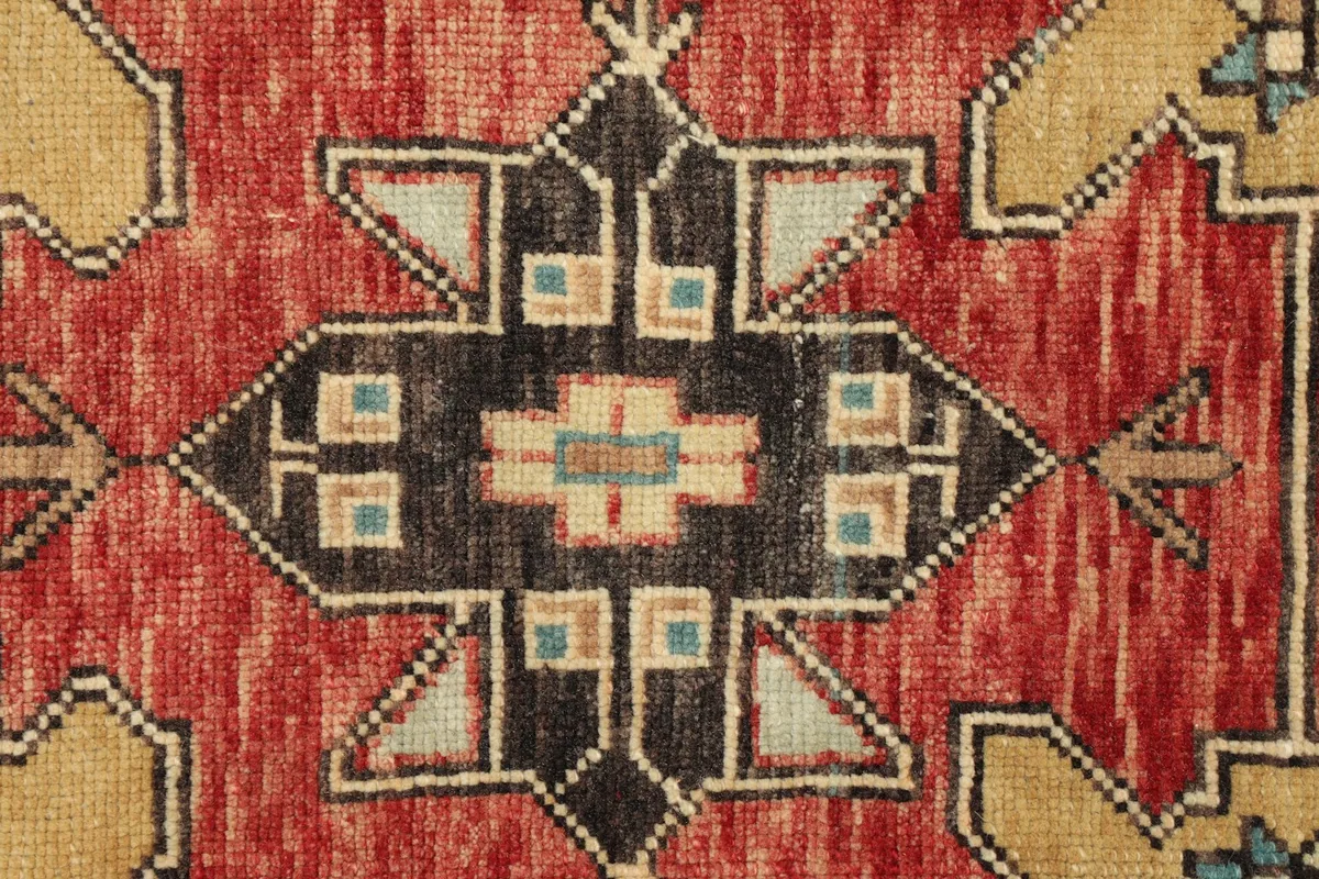 Detailed view of a central tribal geometric motif in charcoal, tan, and ivory on the red field.