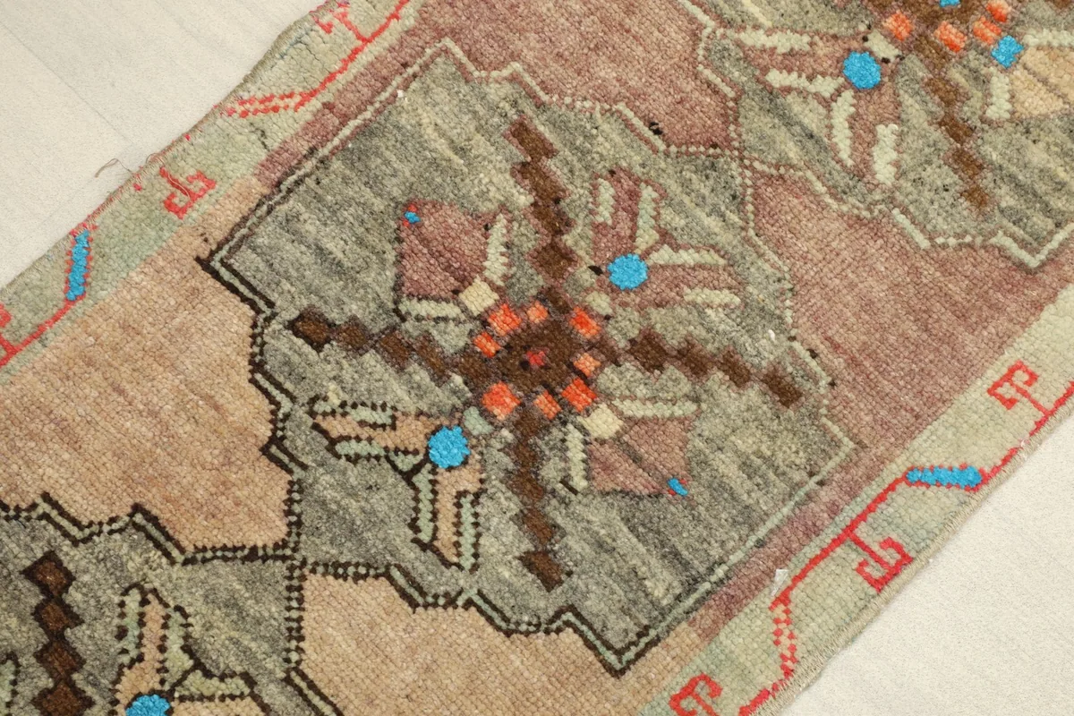 Close-up detail of the vintage rug's tribal geometric motif, highlighting beige, olive, rose, and blue colors.