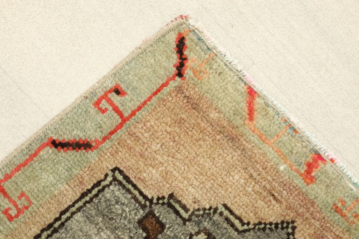 Corner detail of the rug's border, showing the olive green field, beige tones, and red geometric lines.