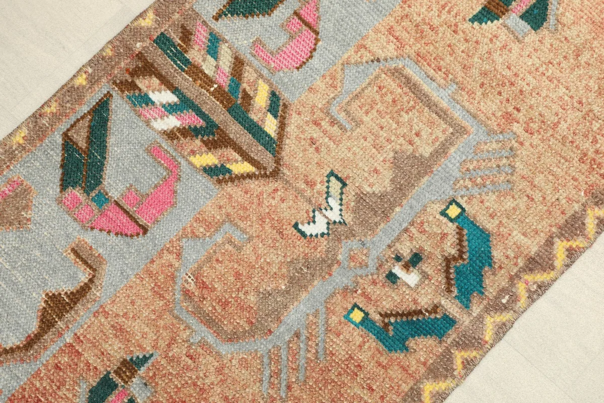Close-up detail of the rug's hand-knotted wool pile and geometric motifs in rust, gray, pink, and green.