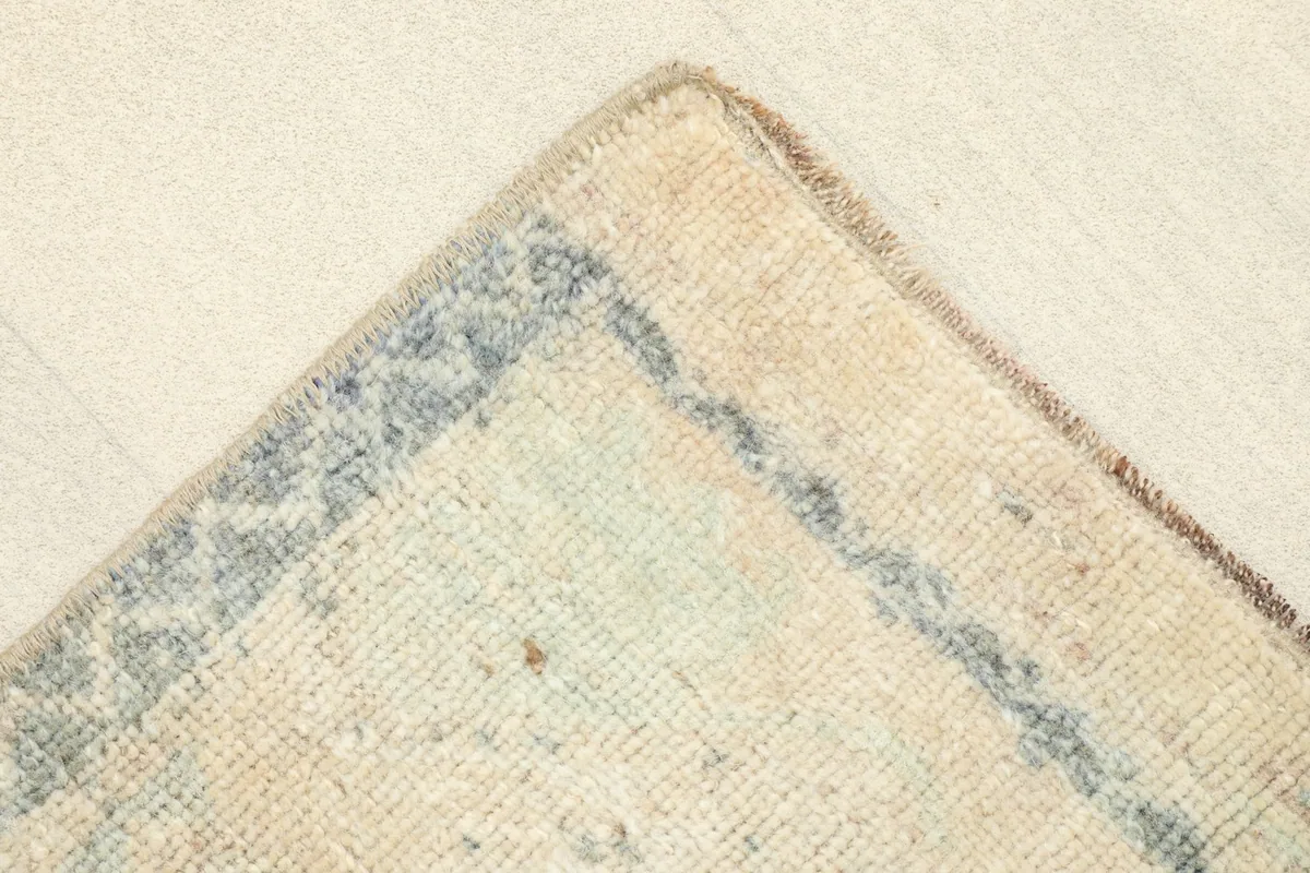 Corner detail of the rug, focusing on the blue geometric border design and the faded ivory field.