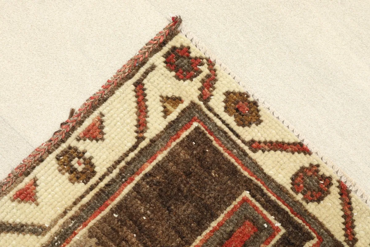 Corner detail showing the beige border with small red and brown tribal motifs, and the hand-knotted edge