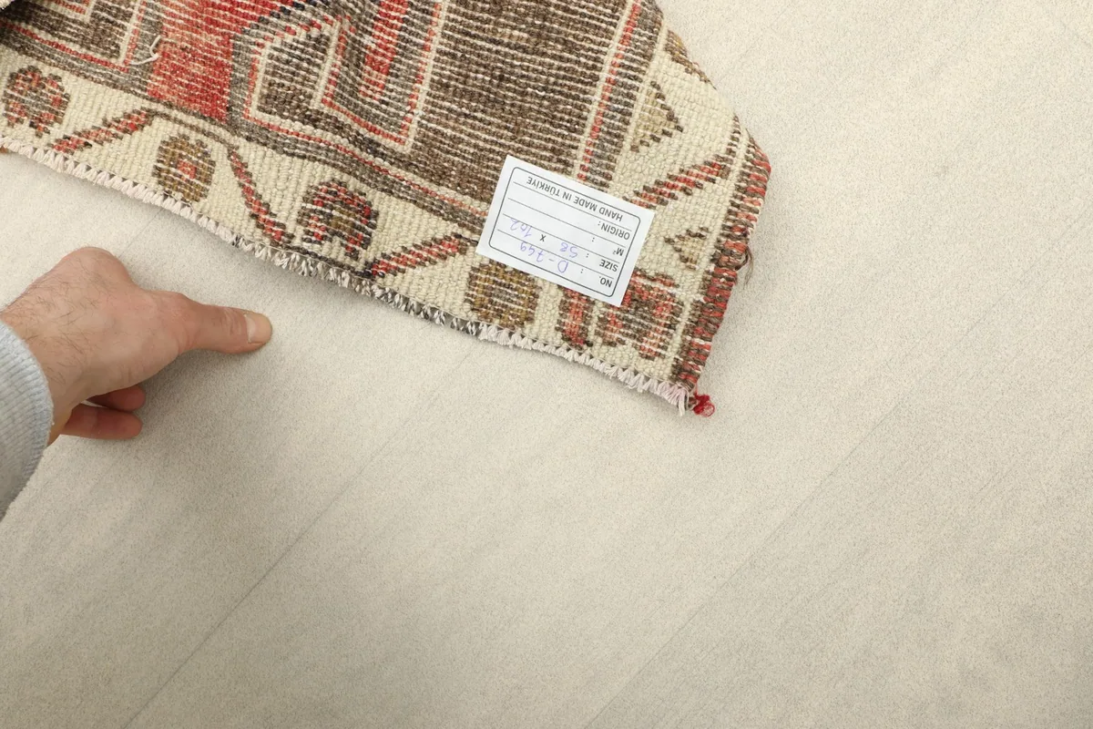A hand holding up a corner of the rug, showing the reverse side with a label and the tight knotting