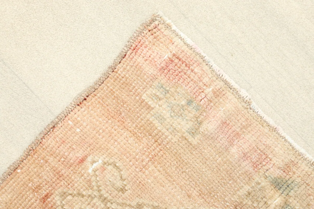 Corner detail of the rug, revealing the subtle pink and rust tones and hand-knotted edges.