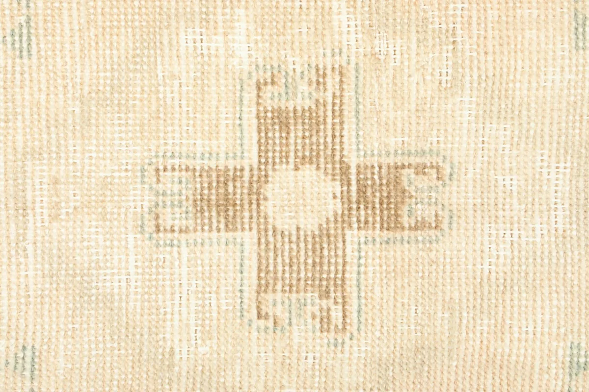 Detailed close-up of the central tan geometric motif on the ivory and beige background of the rug.