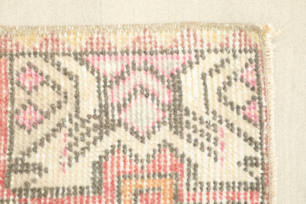 Close-up of the rug's border, featuring intricate geometric motifs in beige, ivory, and gray with a rose background.