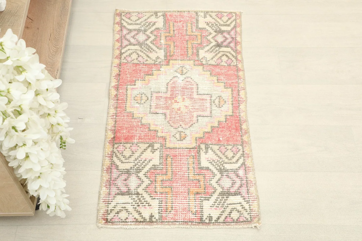 Overhead view of the small rose and ivory vintage rug, showing its full rectangular shape and geometric patterns.