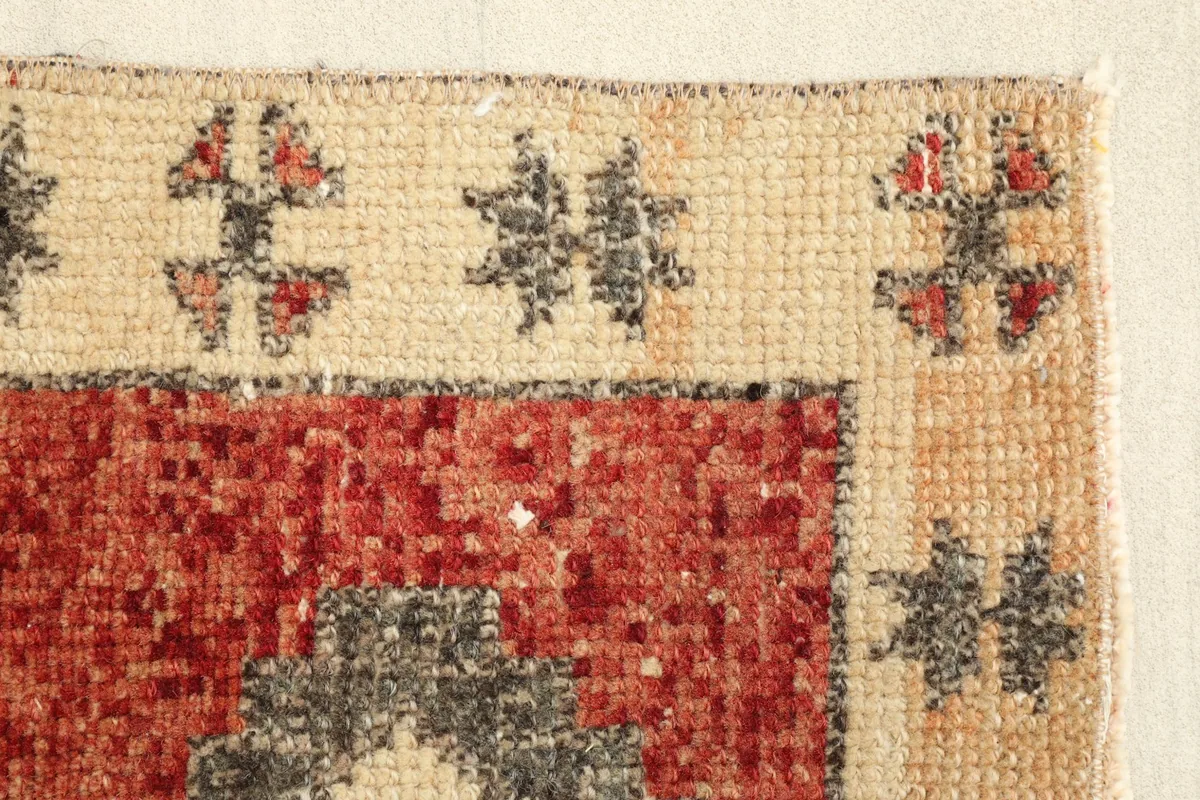 Close-up of the beige border pattern and the textured red pile of the hand-knotted rug