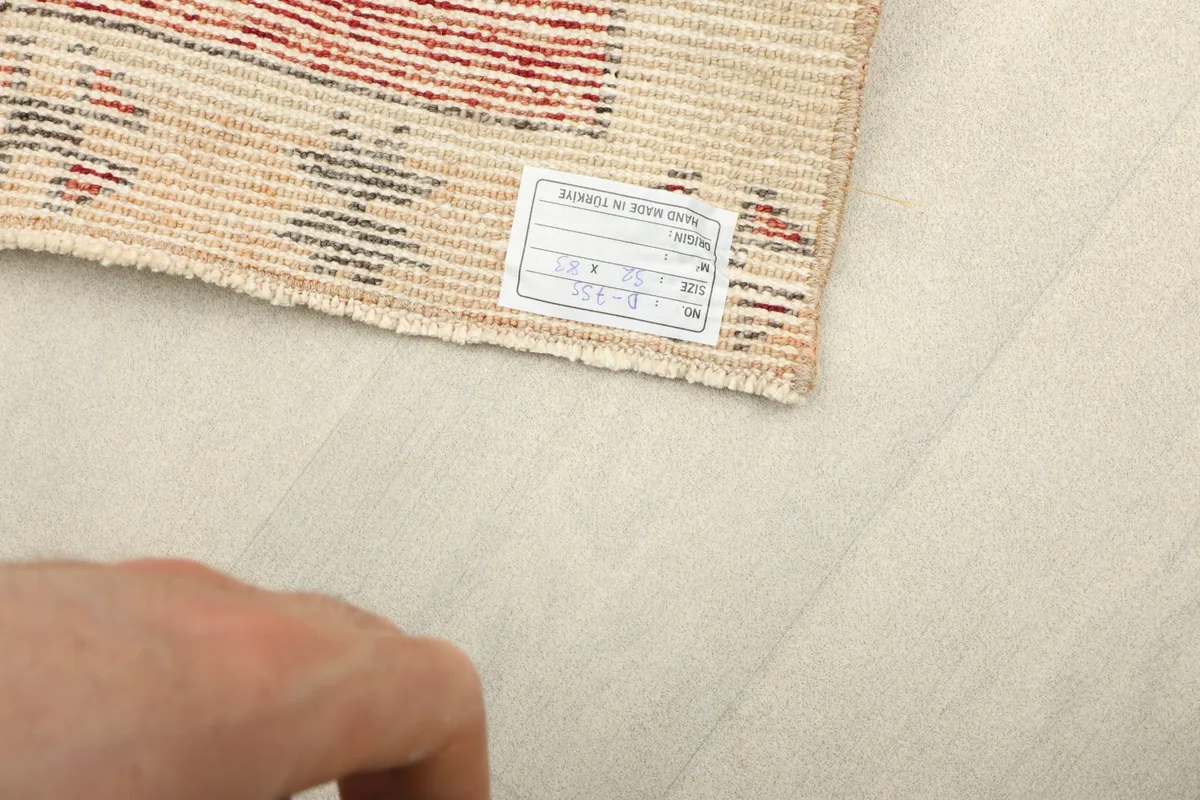 Close-up of the rug's cotton foundation and hand-knotted stitches on the back, with a size label