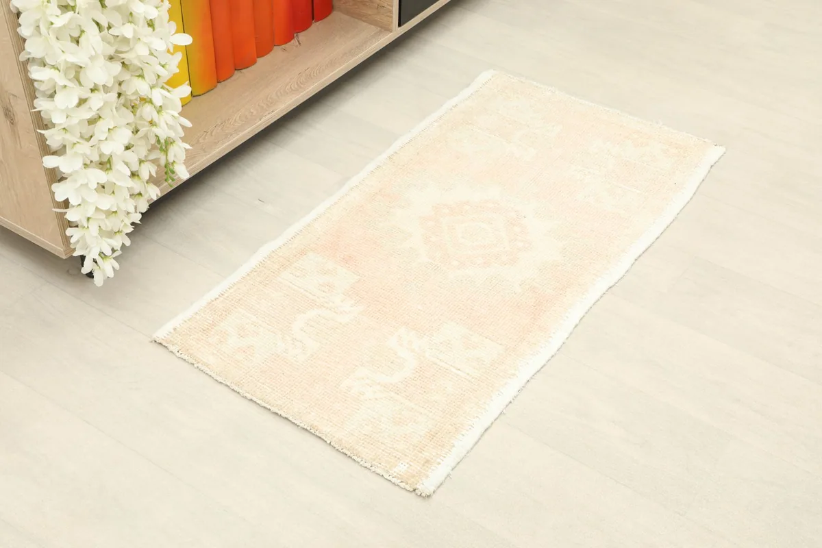 Angle view of the small rose and cream rug on a light floor, next to a shelf.