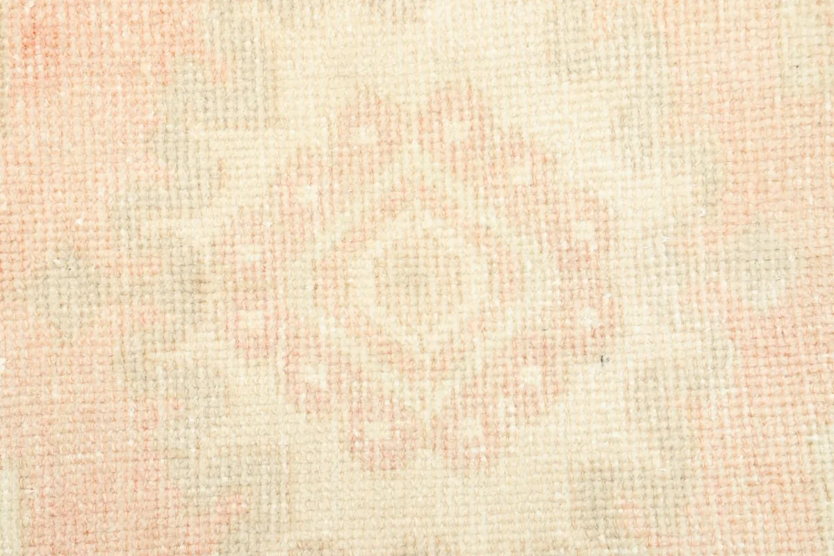 Detailed view of the low wool pile texture and muted rose and cream colors.