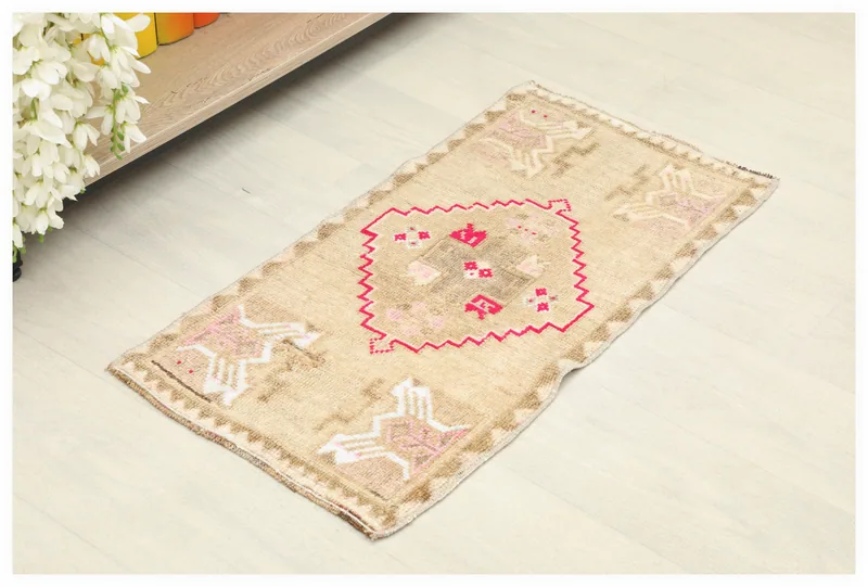 Full top view of a tan and rose vintage Anatolian doormat on a white floor