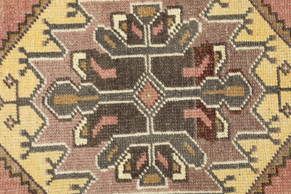 Close-up detail of the central medallion, revealing intricate geometric motifs in pink, yellow, and brown.