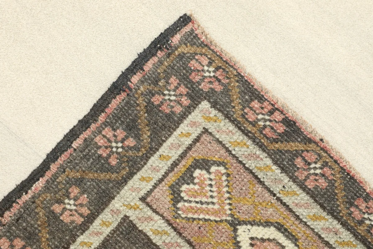 Corner detail of the rug, showing the gray border with pink floral designs and geometric lines.