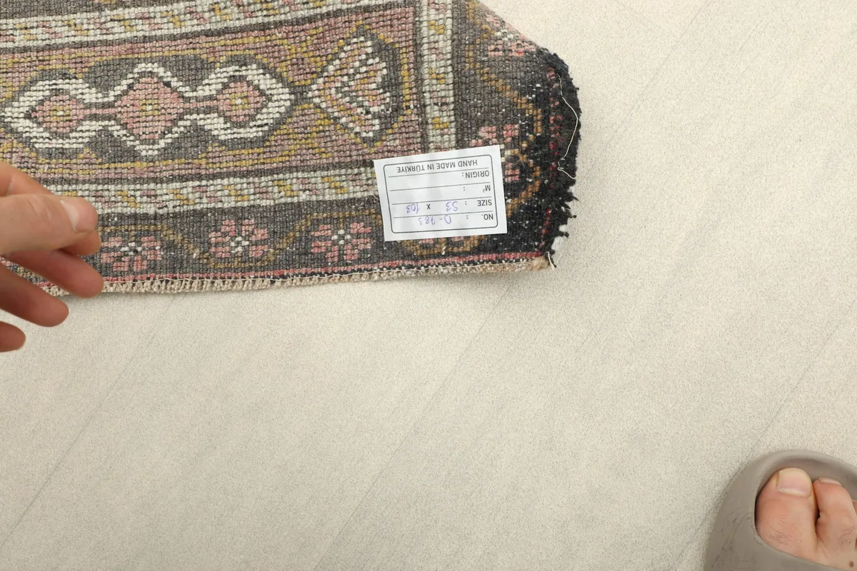 Underside of the rug with a hand holding a label, showing the cotton foundation and knotting.