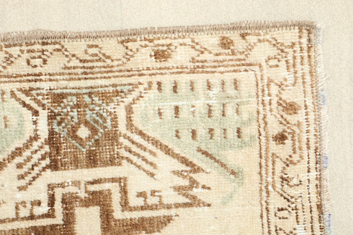 Edge view of the rug, highlighting the worn fringe and the repeating patterns in the brown border.
