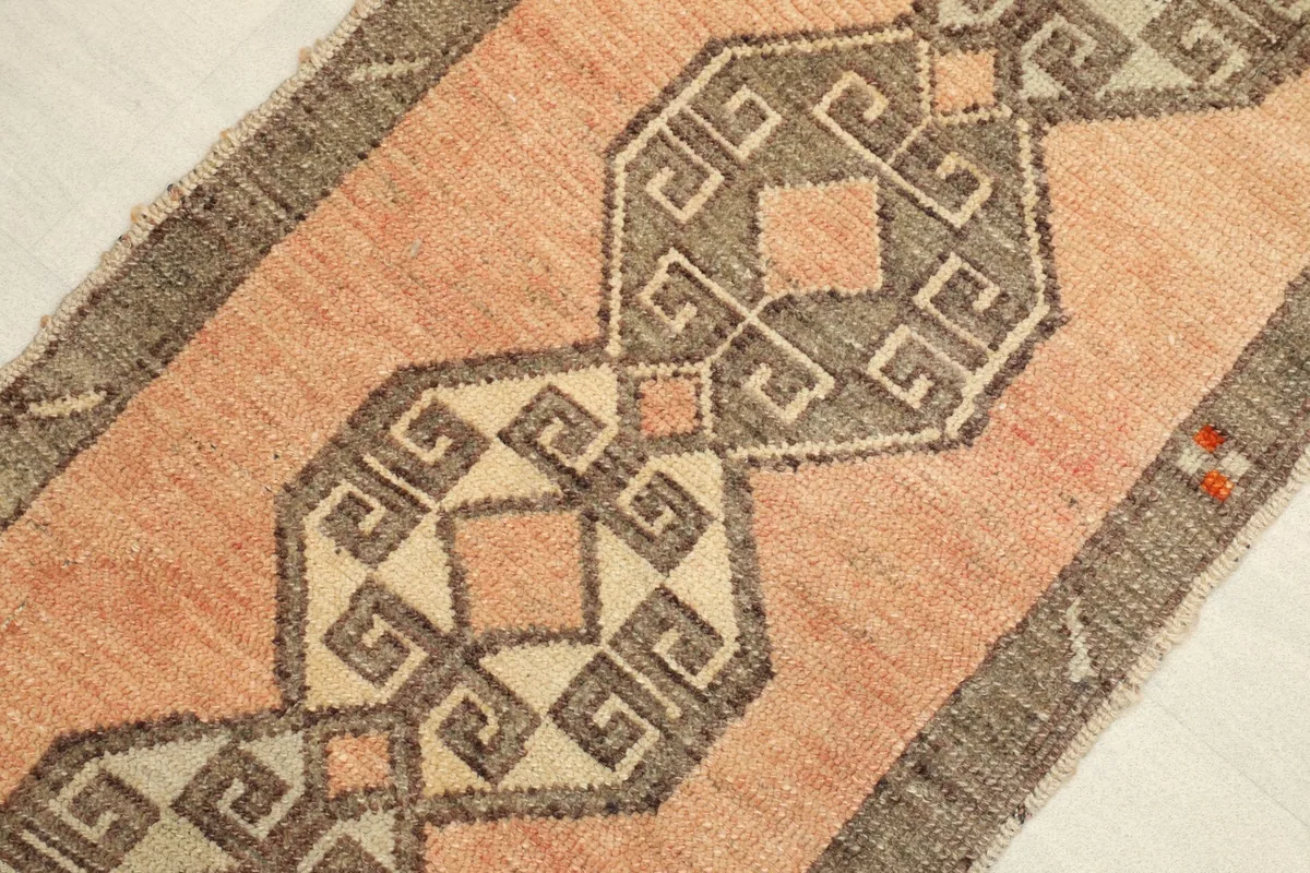 Close-up detail of the central geometric pattern in gray and beige against the orange field.