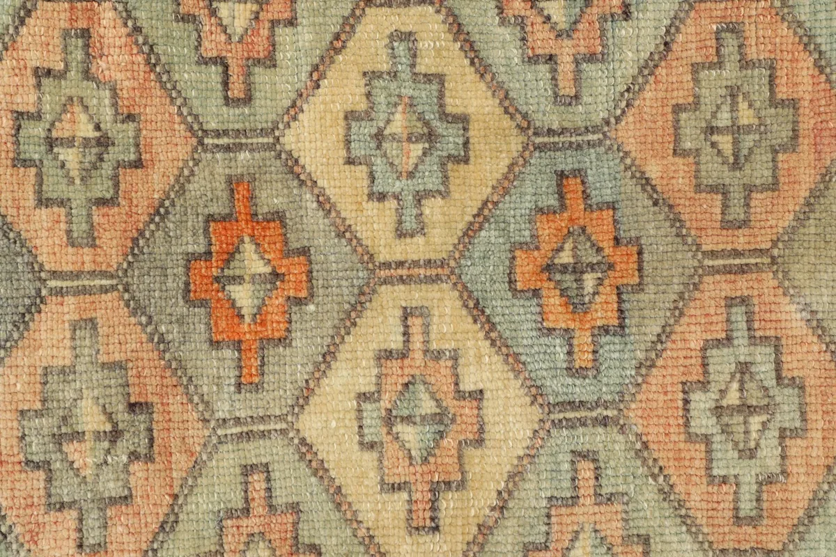 Close-up detail of the hand-knotted wool pile, showing the pale blue, rose, tan, and orange colors.