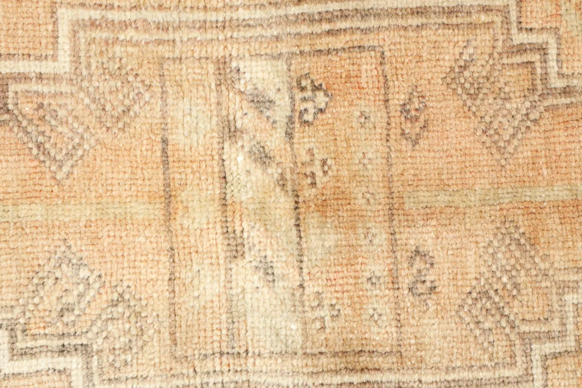 Close-up detail of the central tribal motif and subtle color shifts in the tan and beige wool