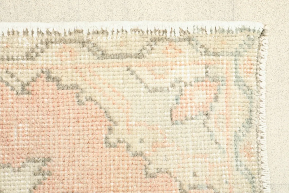 Corner detail of the rug, illustrating the rose field, beige motifs, and the hand-finished edges.