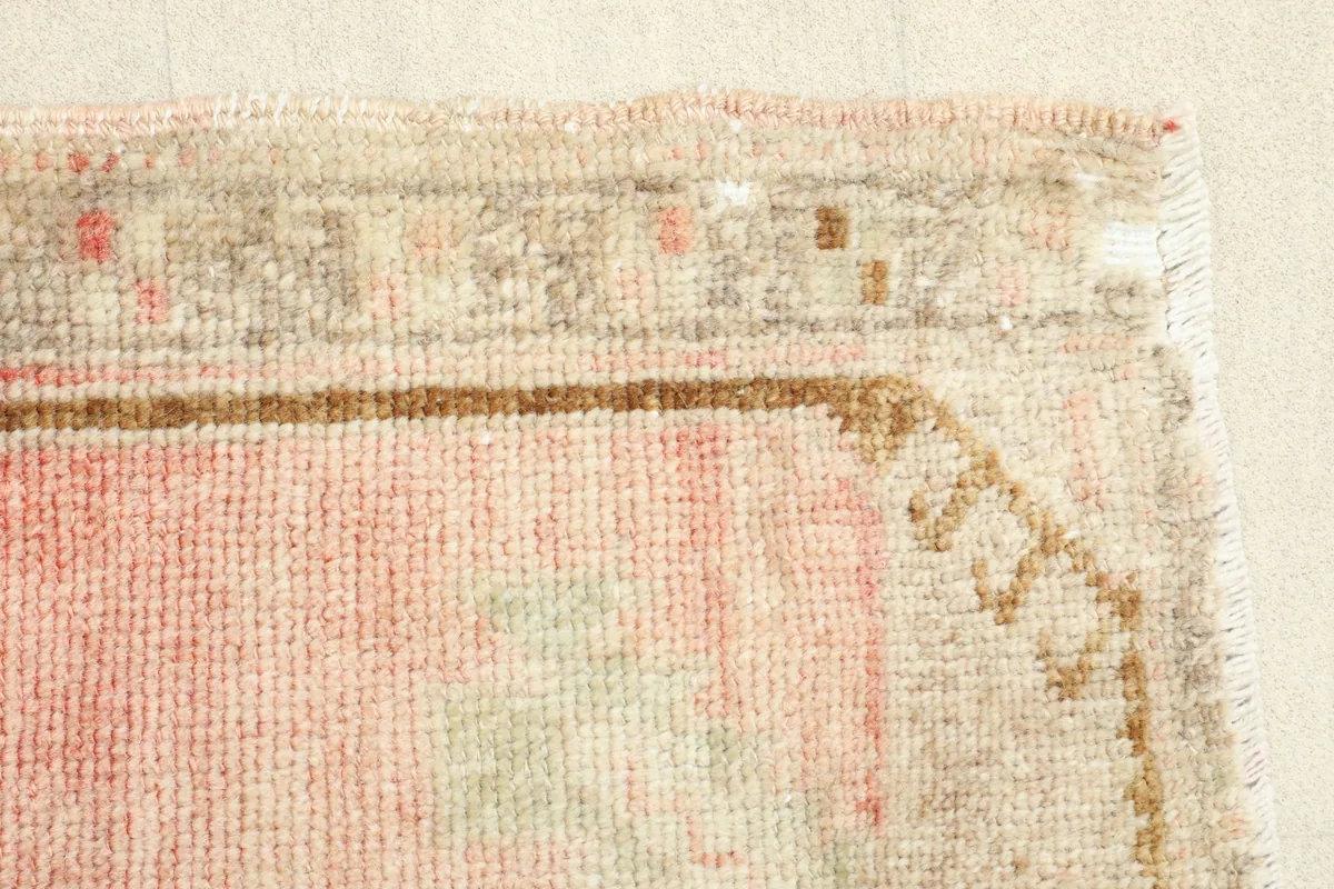 Detail of the rug's edge, revealing the subtle wear and variations in the rose and beige wool pile.