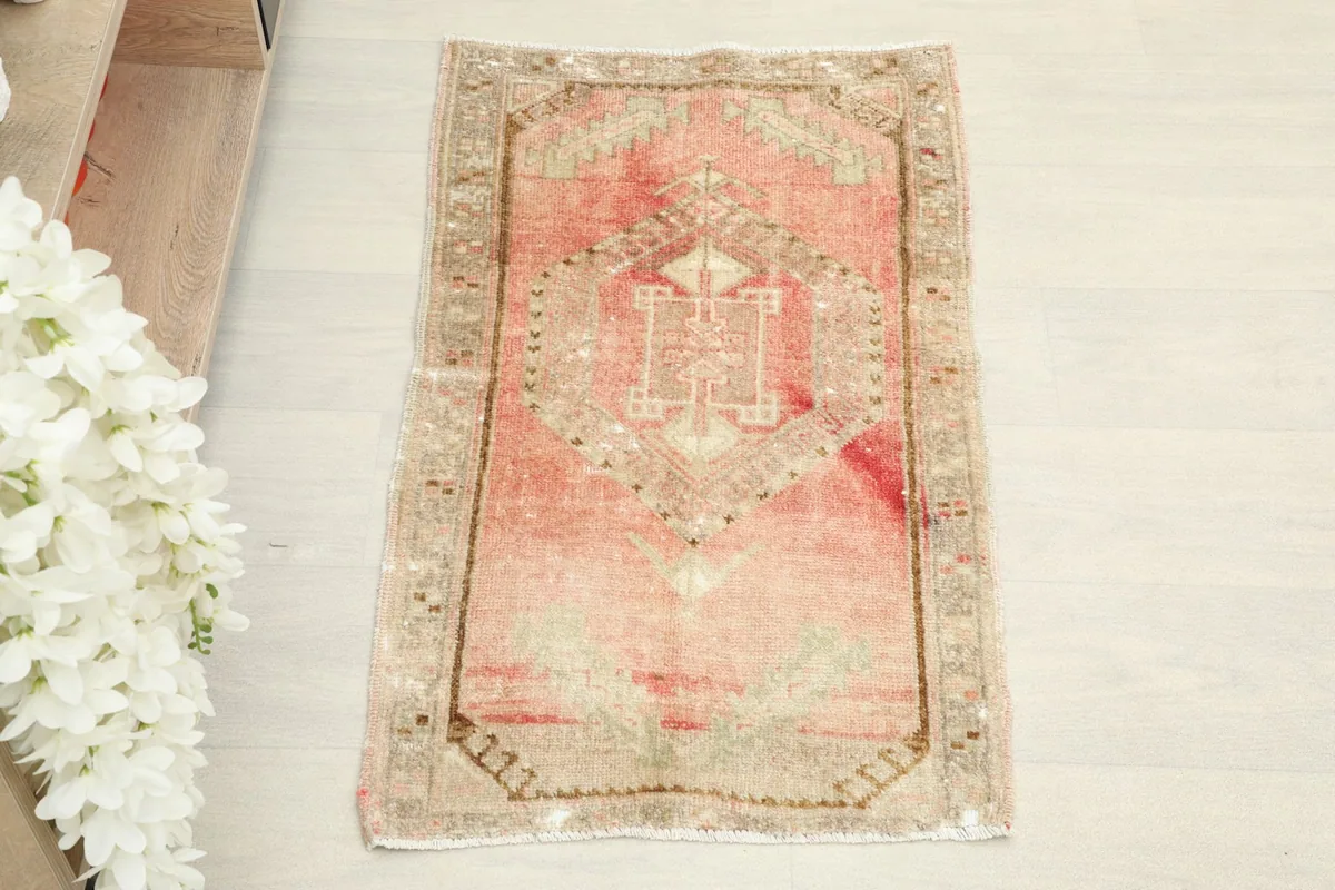Overhead view of the small hand-knotted rug, highlighting its rose field and tribal geometric pattern.